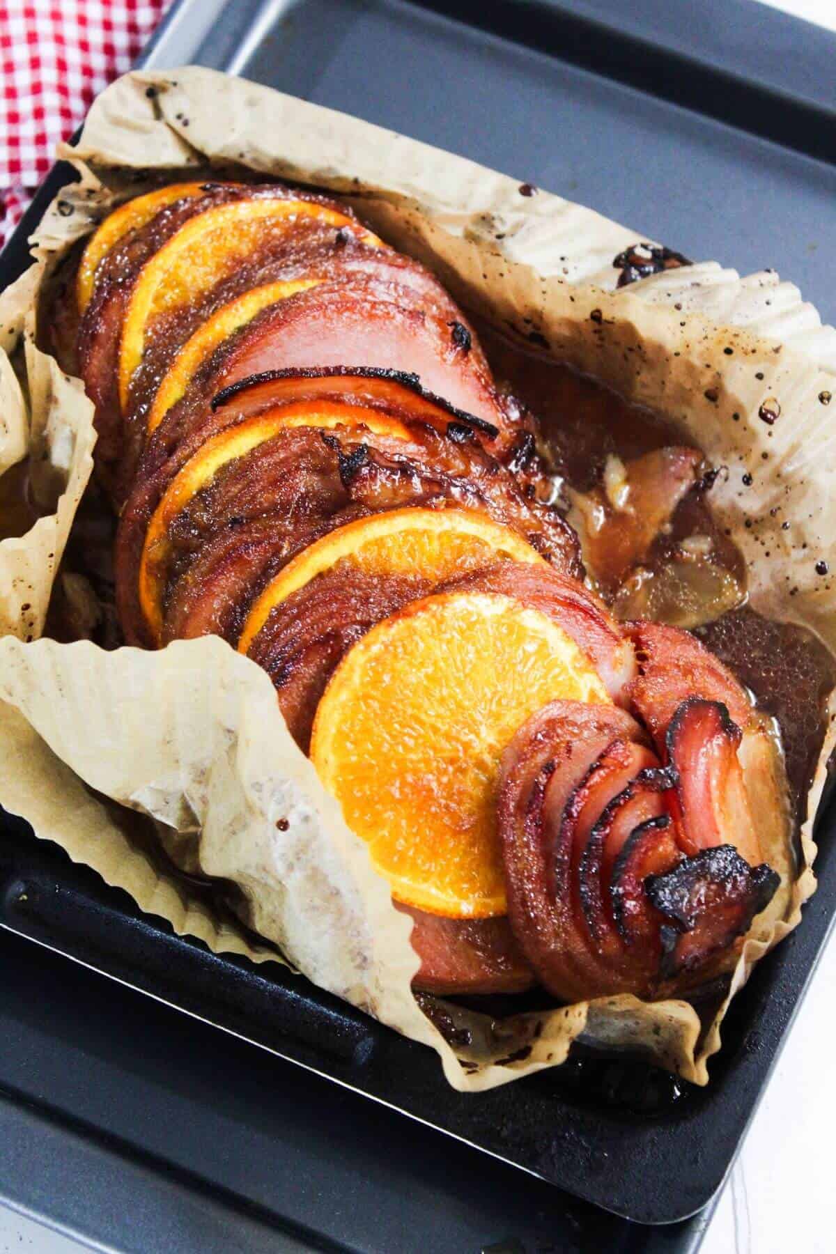 Sliced ham topped with orange slices on parchment paper in a baking tray.