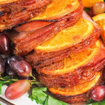 Sliced ham with orange slices and grapes, garnished with parsley on a platter.