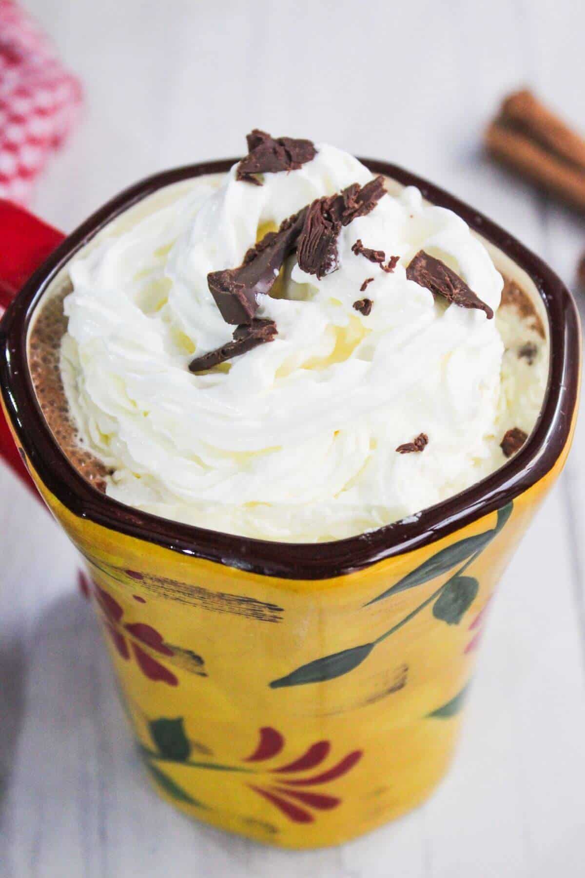 A yellow floral mug filled with hot chocolate topped with whipped cream and chocolate shavings.
