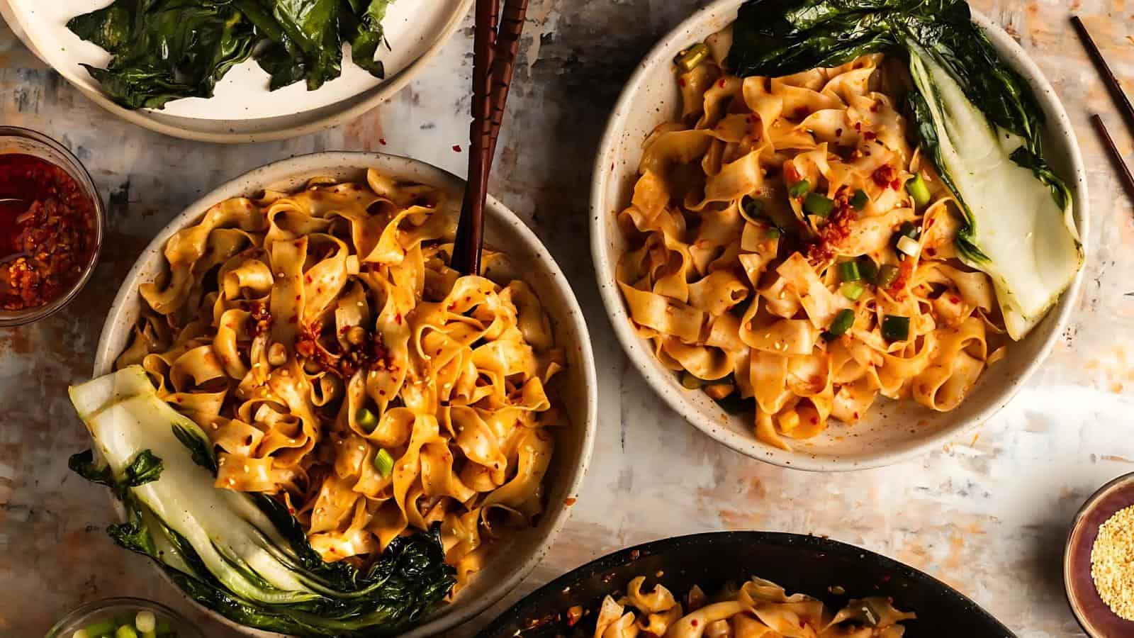 Bowls of spicy noodles with bok choy, garnished with chopped green onions and chili flakes.