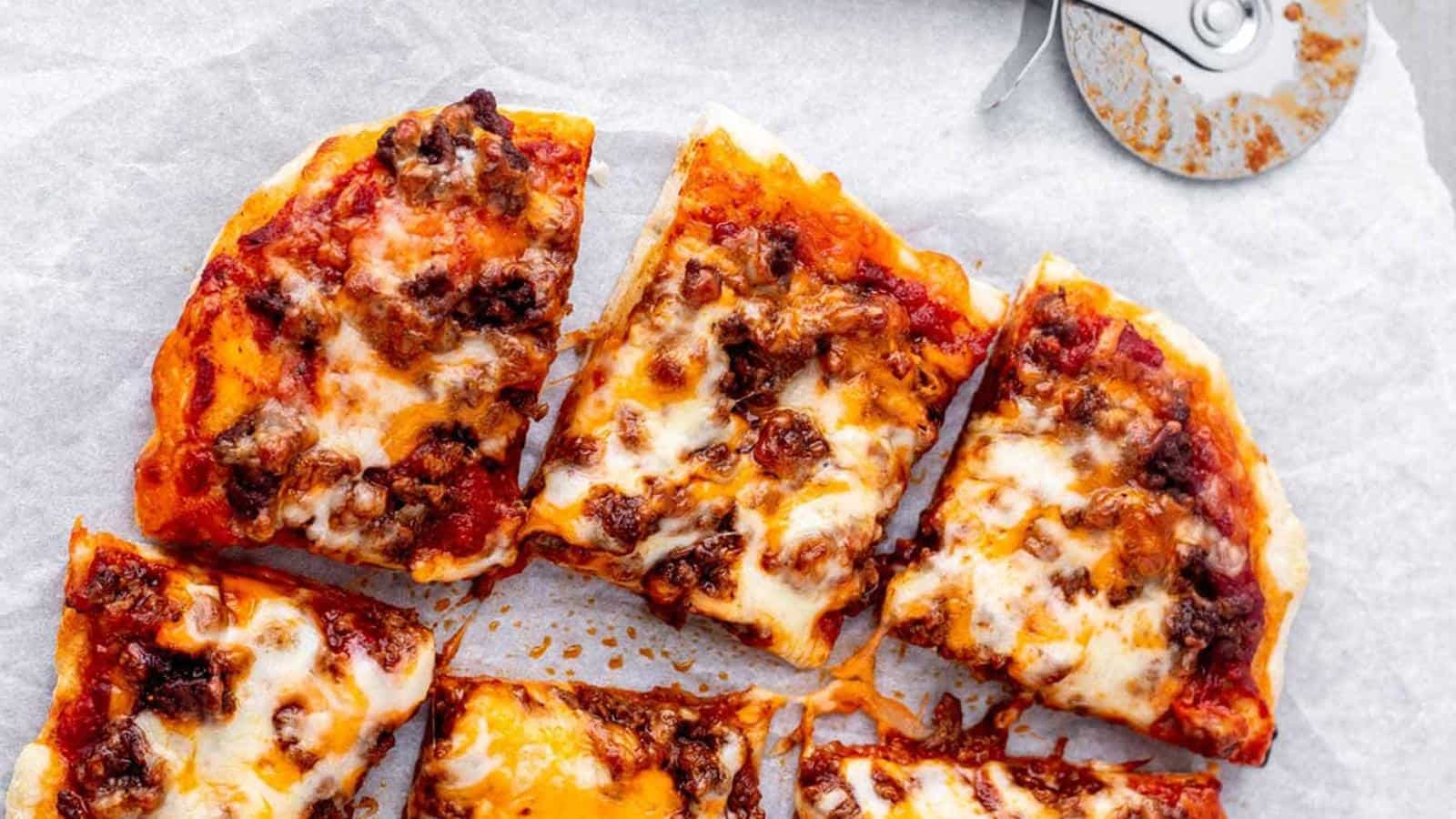 Slices of pizza with cheese and meat toppings on parchment paper, next to a pizza cutter.