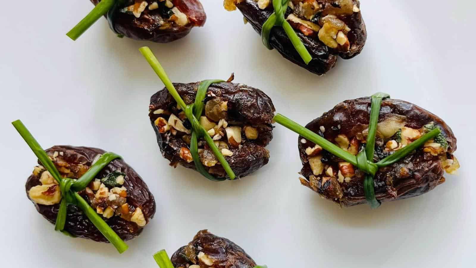 Six stuffed dates wrapped in chive strands on a white background.