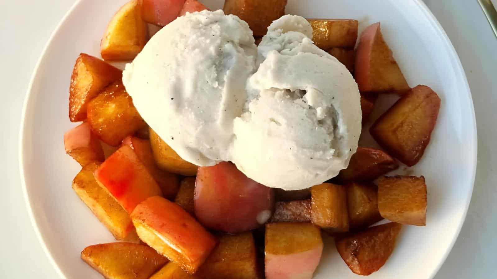 A plate of caramelized apple and peach pieces topped with two scoops of vanilla ice cream.