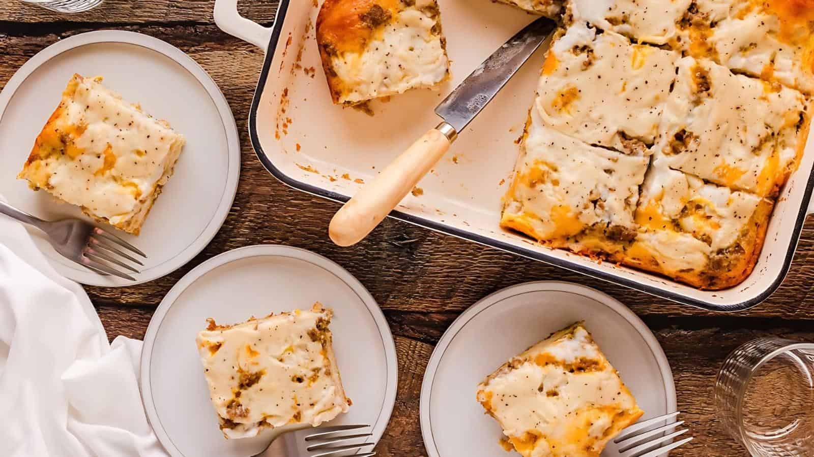 Slices of lasagna served on three plates, with a baking dish of lasagna partially cut, set on a wooden table.