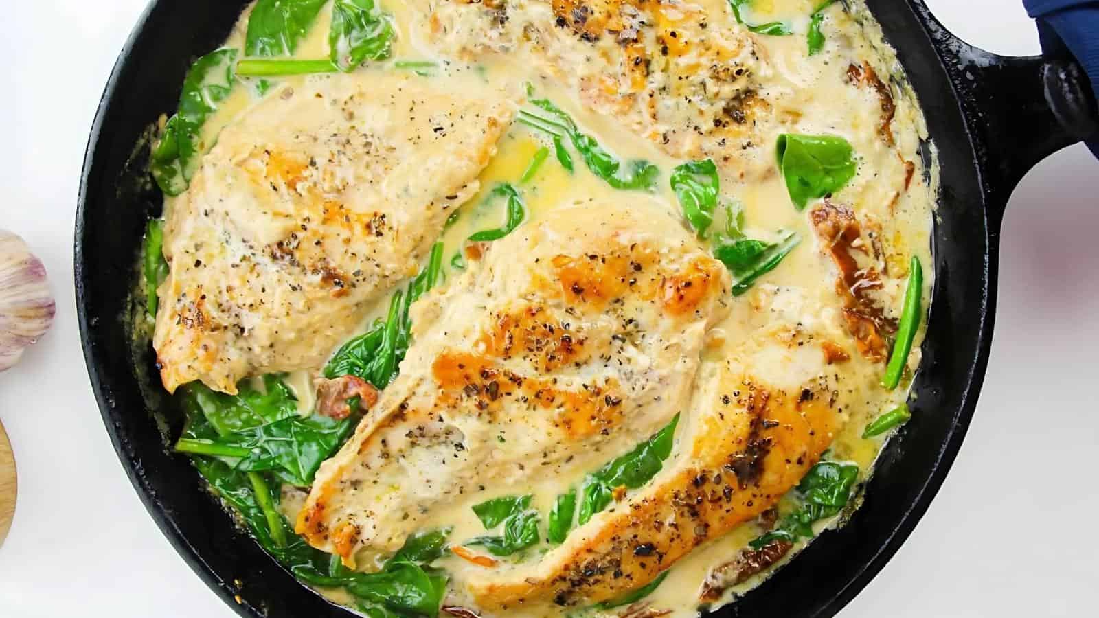 A skillet with creamy garlic chicken, spinach, and a light sauce.