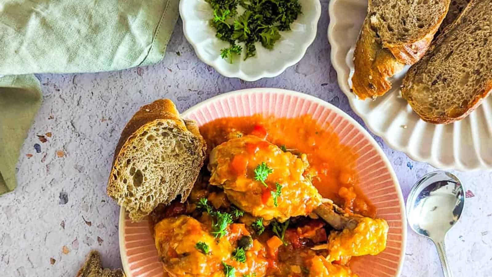 Plate of chicken stew with vegetables, garnished with parsley, accompanied by slices of bread.