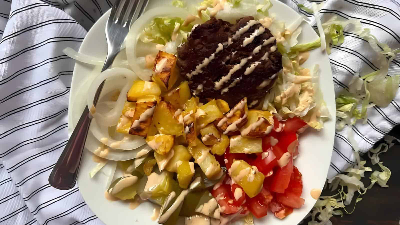 A plate of grilled patty with pineapple, tomato, onion, and cucumber slices. Drizzled with sauce, and set on a striped cloth.