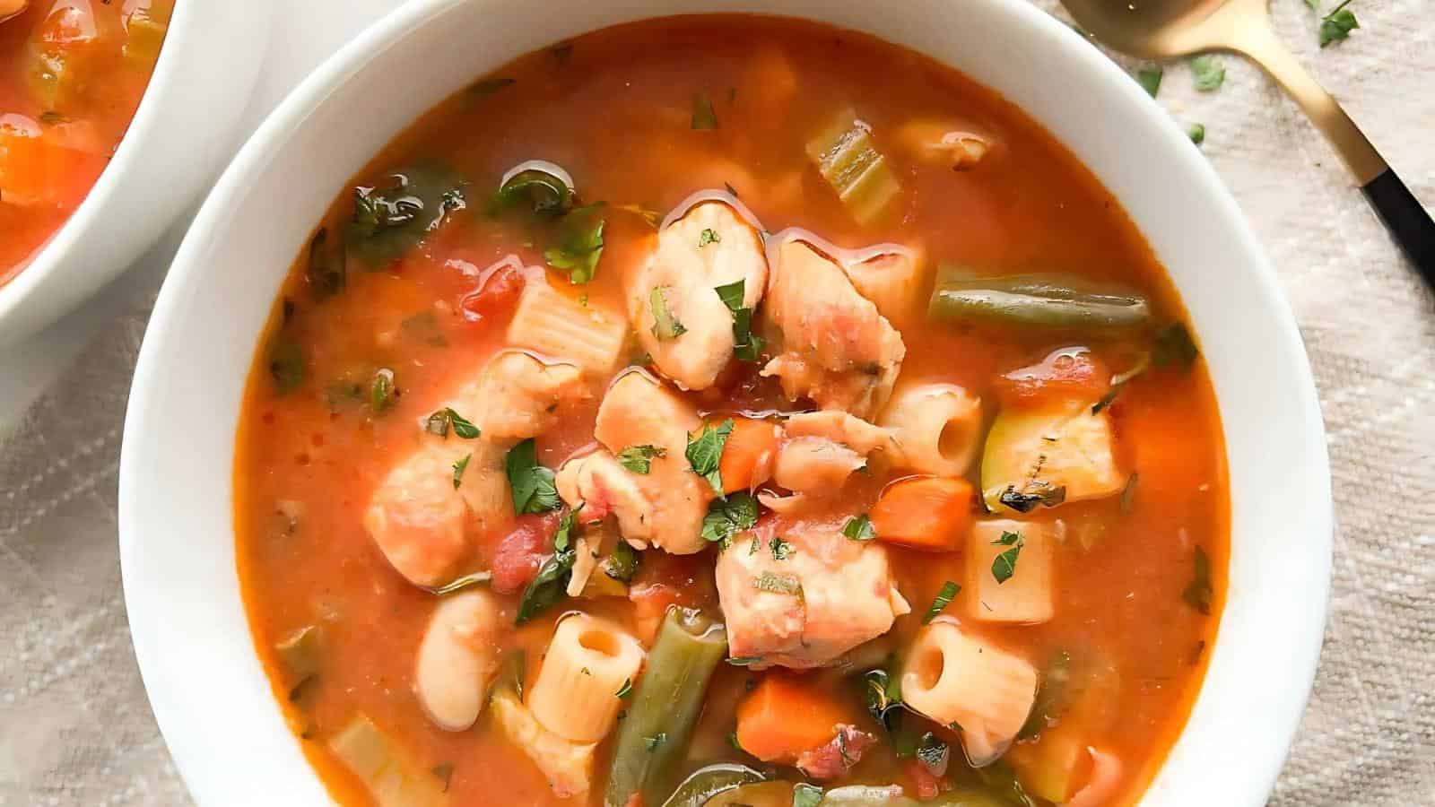 A bowl of vegetable and chicken soup with pasta, garnished with chopped herbs.