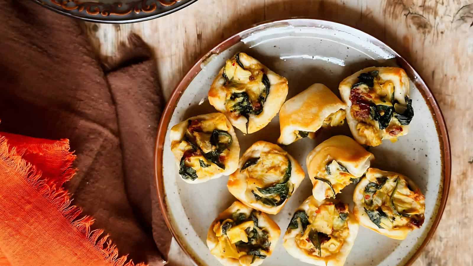 A plate of savory pastries filled with spinach and cheese, arranged on a wooden table with orange and brown cloth napkins nearby.