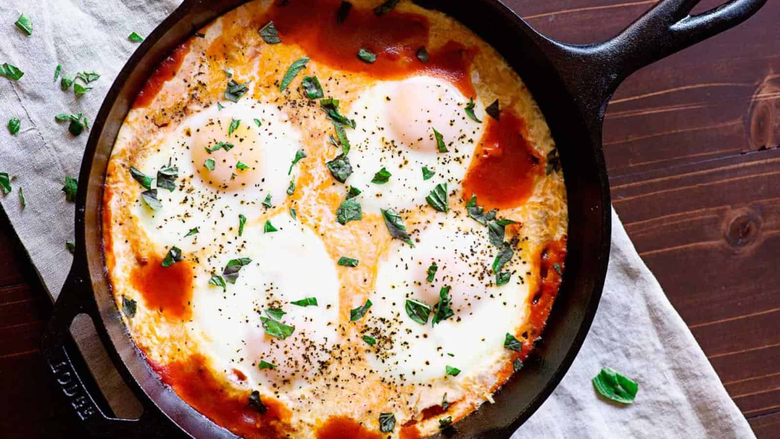 A cast iron skillet containing baked eggs in a tomato sauce, garnished with chopped herbs, on a wooden table.