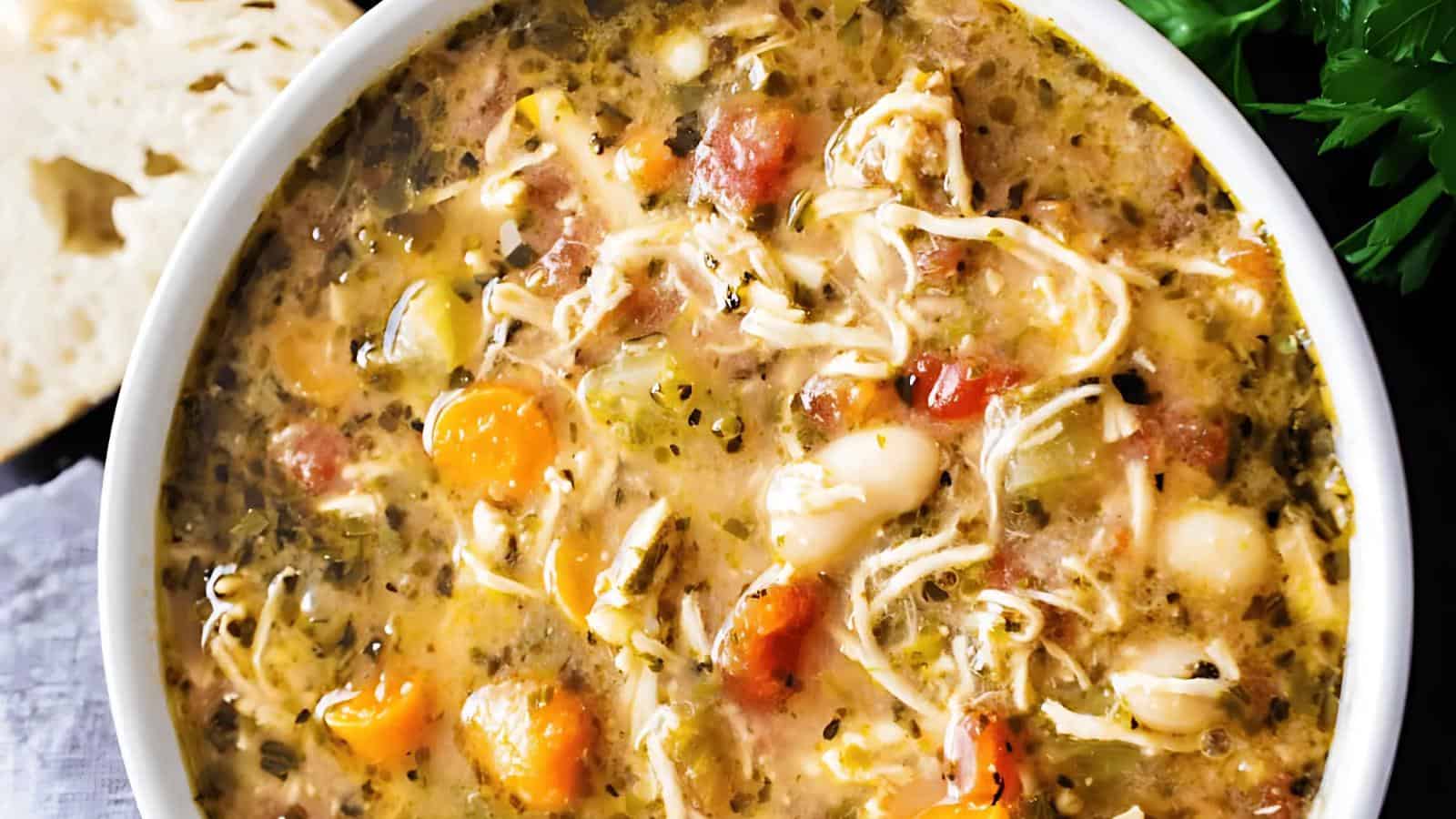 A bowl of chicken and vegetable soup with shredded chicken, tomatoes, beans, carrots, and herbs visible.