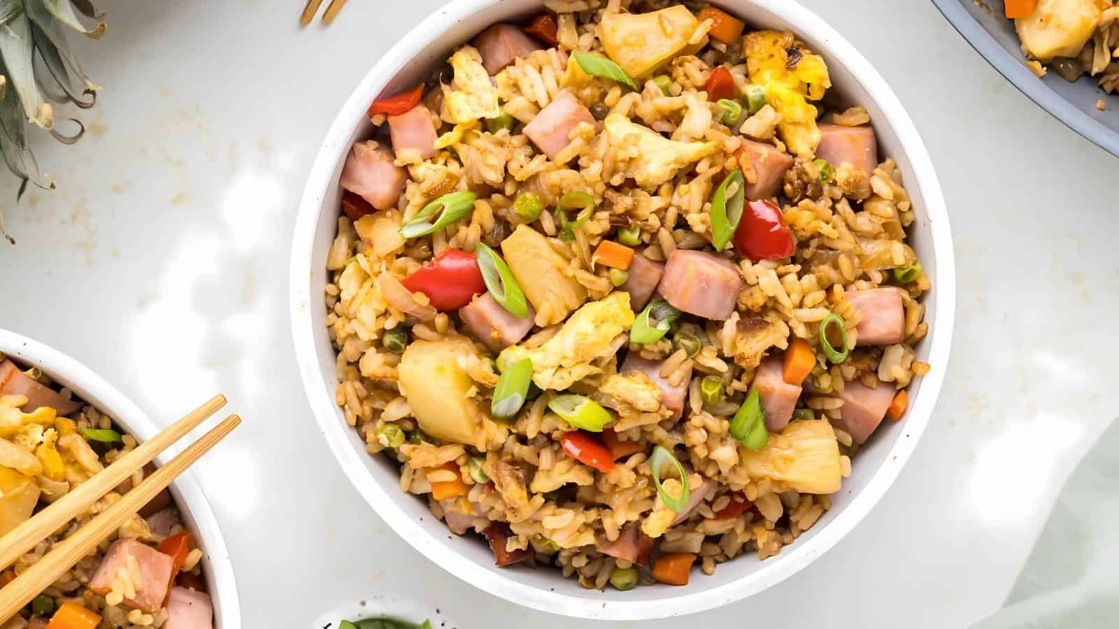 A bowl of pineapple fried rice with ham, eggs, peas, red bell pepper, carrots, and green onions.