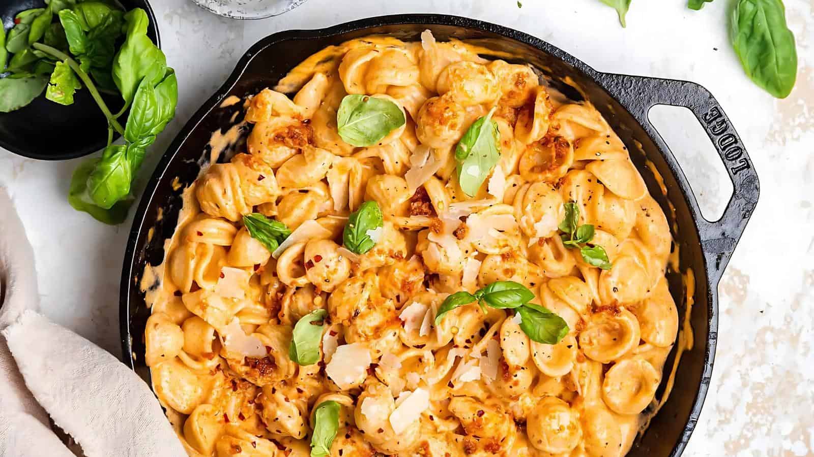A skillet with creamy pasta topped with basil leaves and grated cheese.