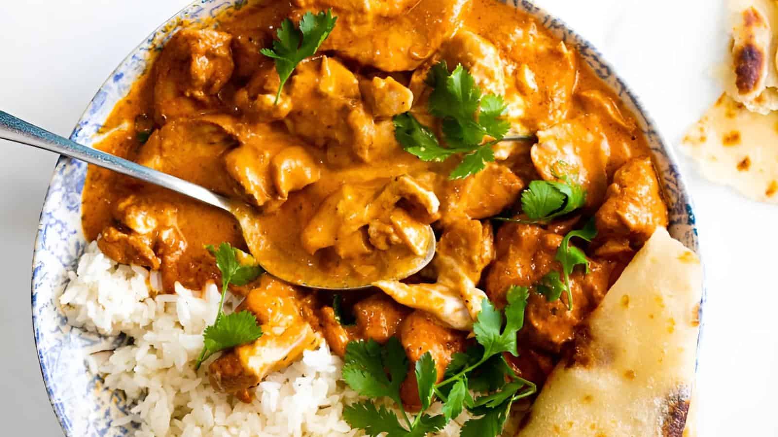 A plate of chicken curry with rice and naan, garnished with cilantro.