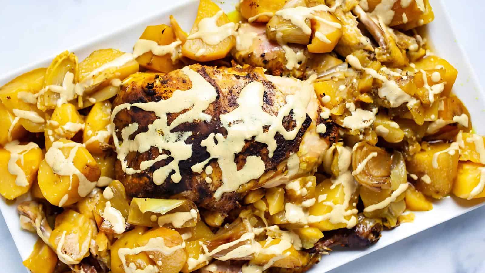 A roasted chicken breast covered in sauce is surrounded by potatoes and vegetables on a rectangular white plate.