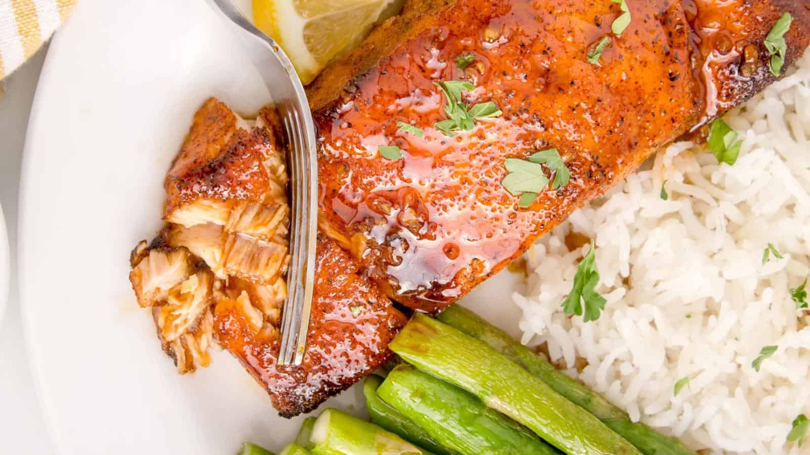 Grilled salmon with herbs, served with white rice, asparagus, and a lemon wedge on the side.