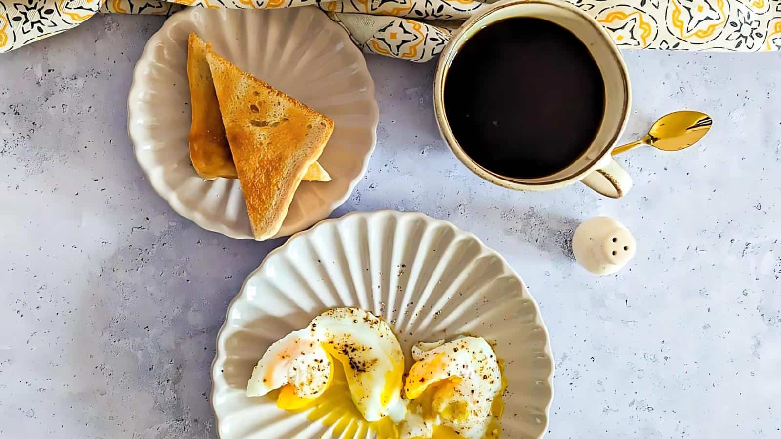 Two poached eggs on a plate, two pieces of toast on a separate plate, and a cup of black coffee with a spoon on a light surface.
