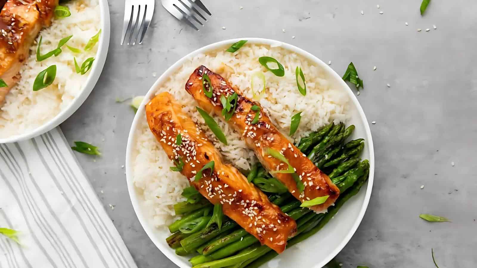 A plate with grilled salmon, asparagus, and rice garnished with green onions and sesame seeds.