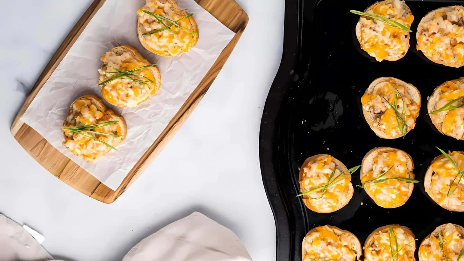 Toasted bread slices topped with shredded cheese and herbs on a wooden board and black tray.