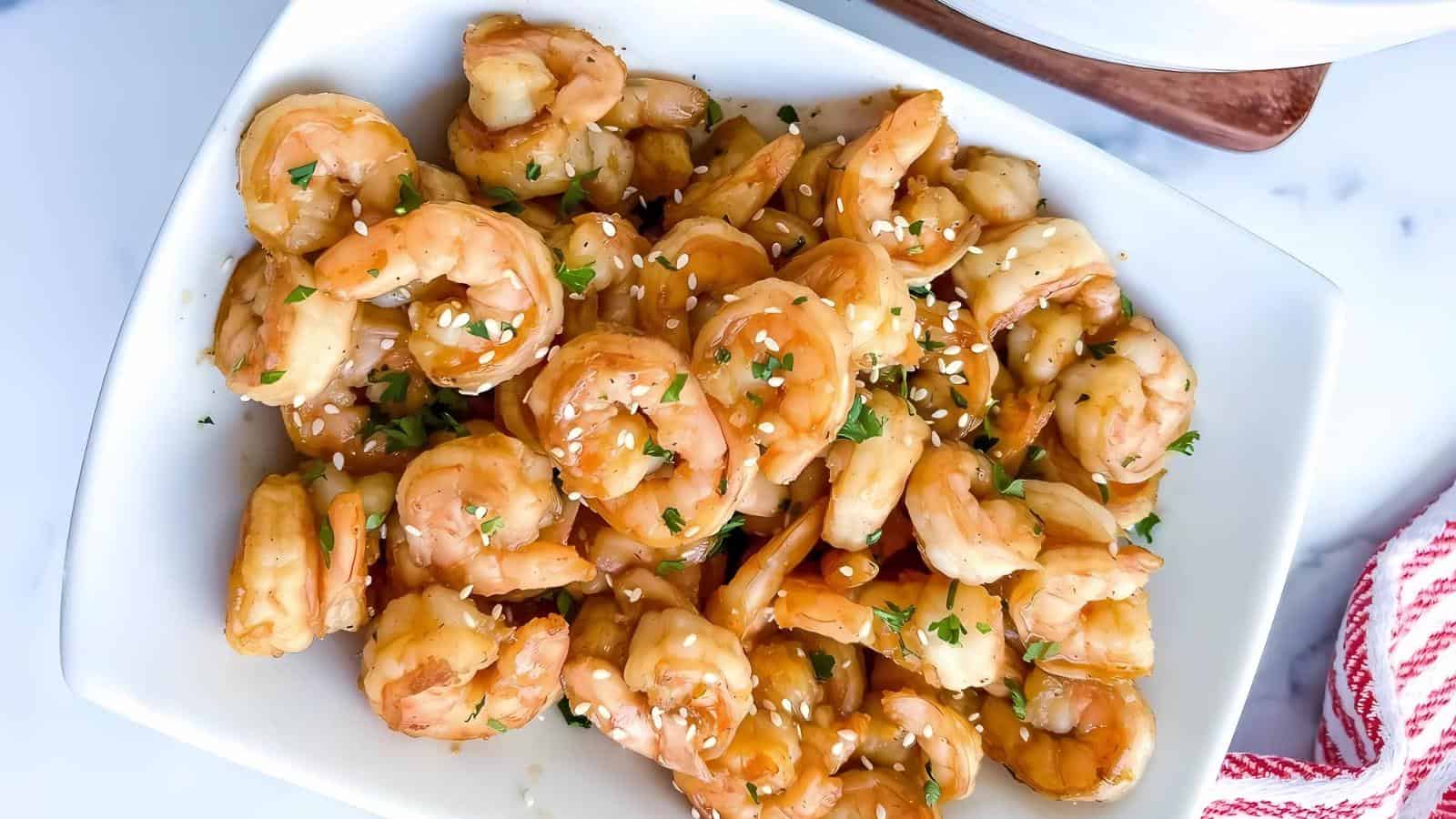A plate of cooked shrimp topped with sesame seeds and parsley, set on a white table.