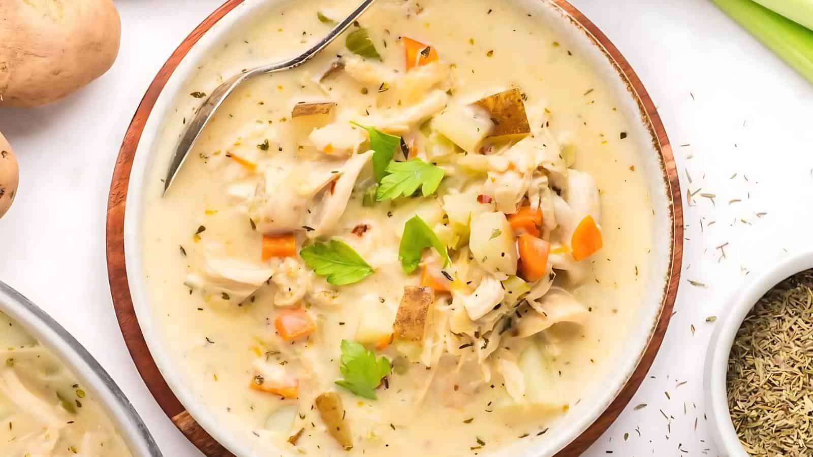 A bowl of creamy soup with chunks of vegetables and herbs, garnished with fresh parsley, and a spoon resting inside.