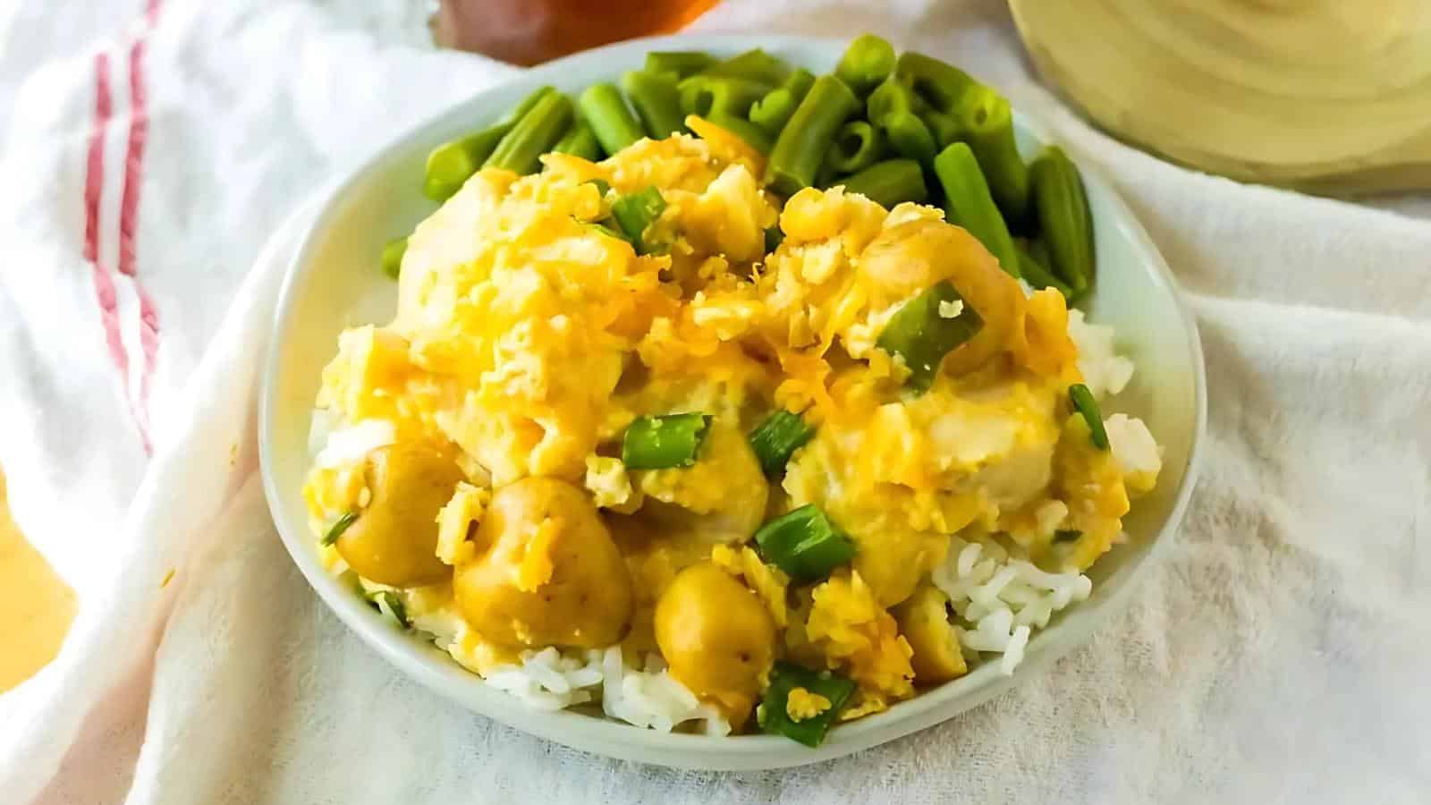 A plate of rice topped with chicken and yellow sauce, garnished with green beans and diced green onions.
