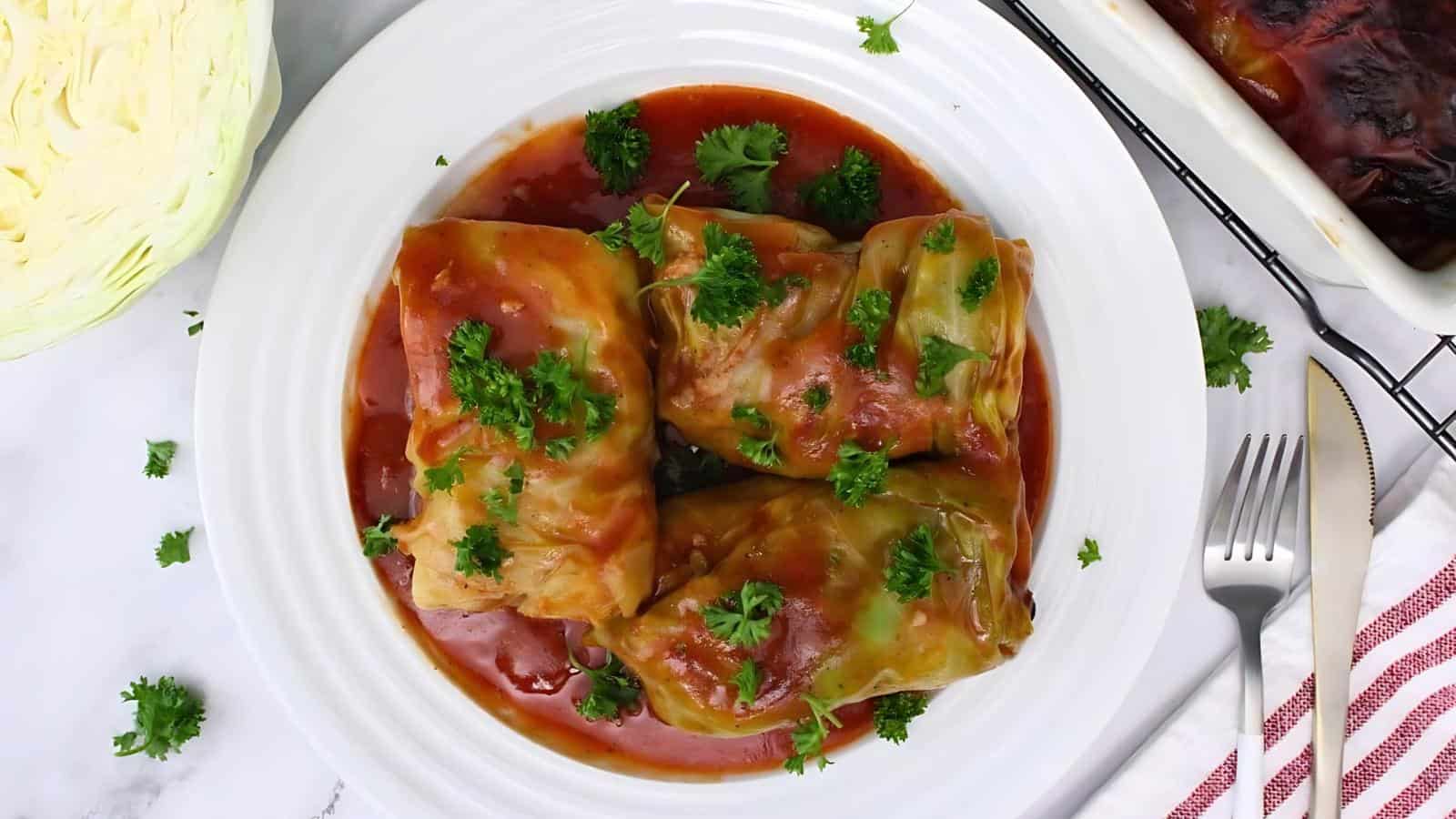 A plate of cabbage rolls topped with tomato sauce and garnished with parsley, served on a white plate.