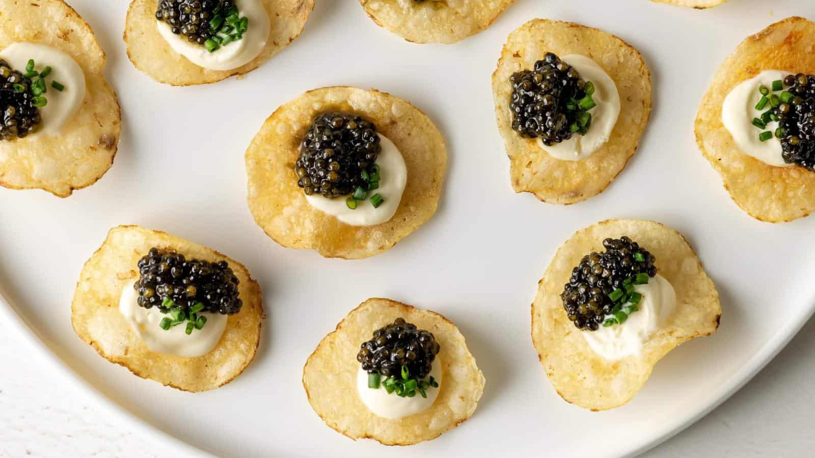 Potato chips topped with dollops of cream, black caviar, and chopped chives arranged on a white plate.
