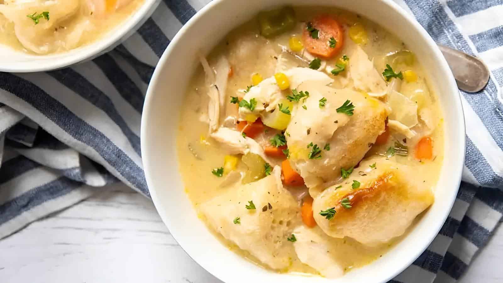 Bowl of chicken and dumplings soup with vegetables, garnished with parsley, on a striped cloth.