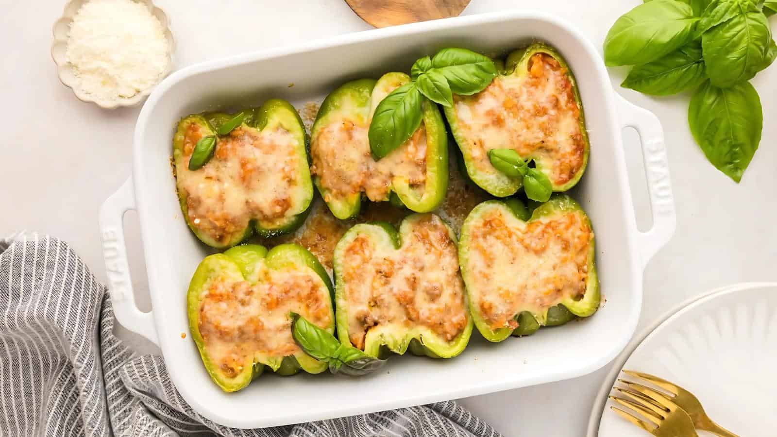 Baked stuffed green peppers with melted cheese in a white dish, garnished with fresh basil leaves.