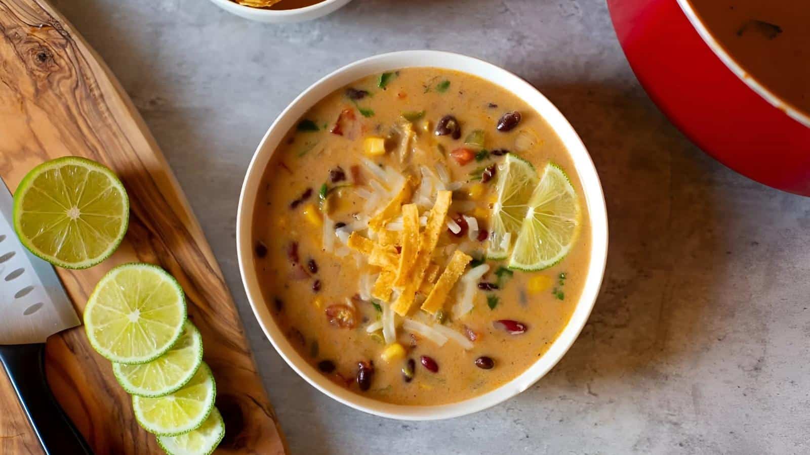 A bowl of soup with black beans, corn, cheese, and tortilla strips, garnished with lime slices.