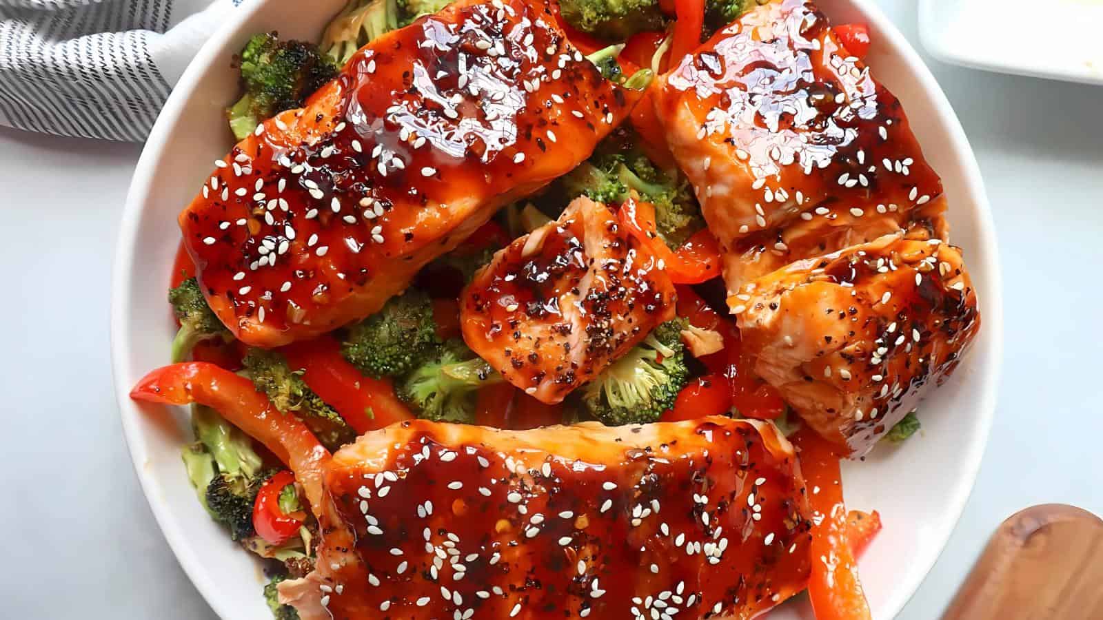 A plate of glazed salmon topped with sesame seeds, served over broccoli and red bell peppers.