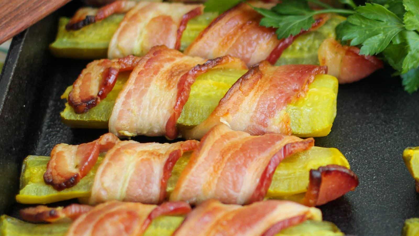 Bacon-wrapped pickles on a black tray, garnished with fresh parsley.