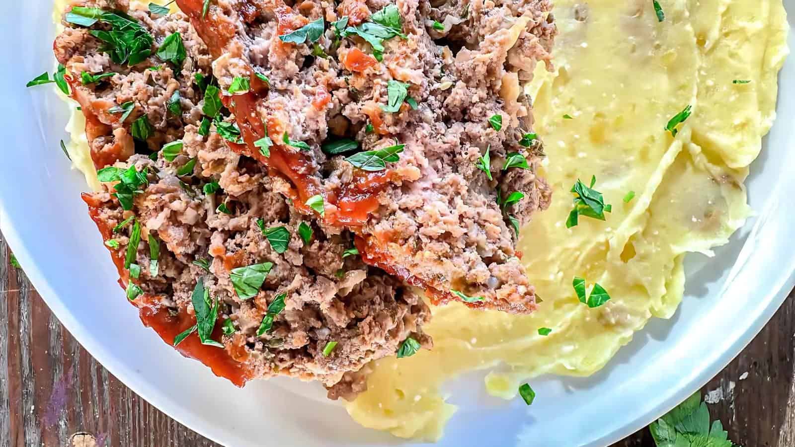 A plate of meatloaf topped with sauce and herbs, served alongside creamy mashed potatoes.