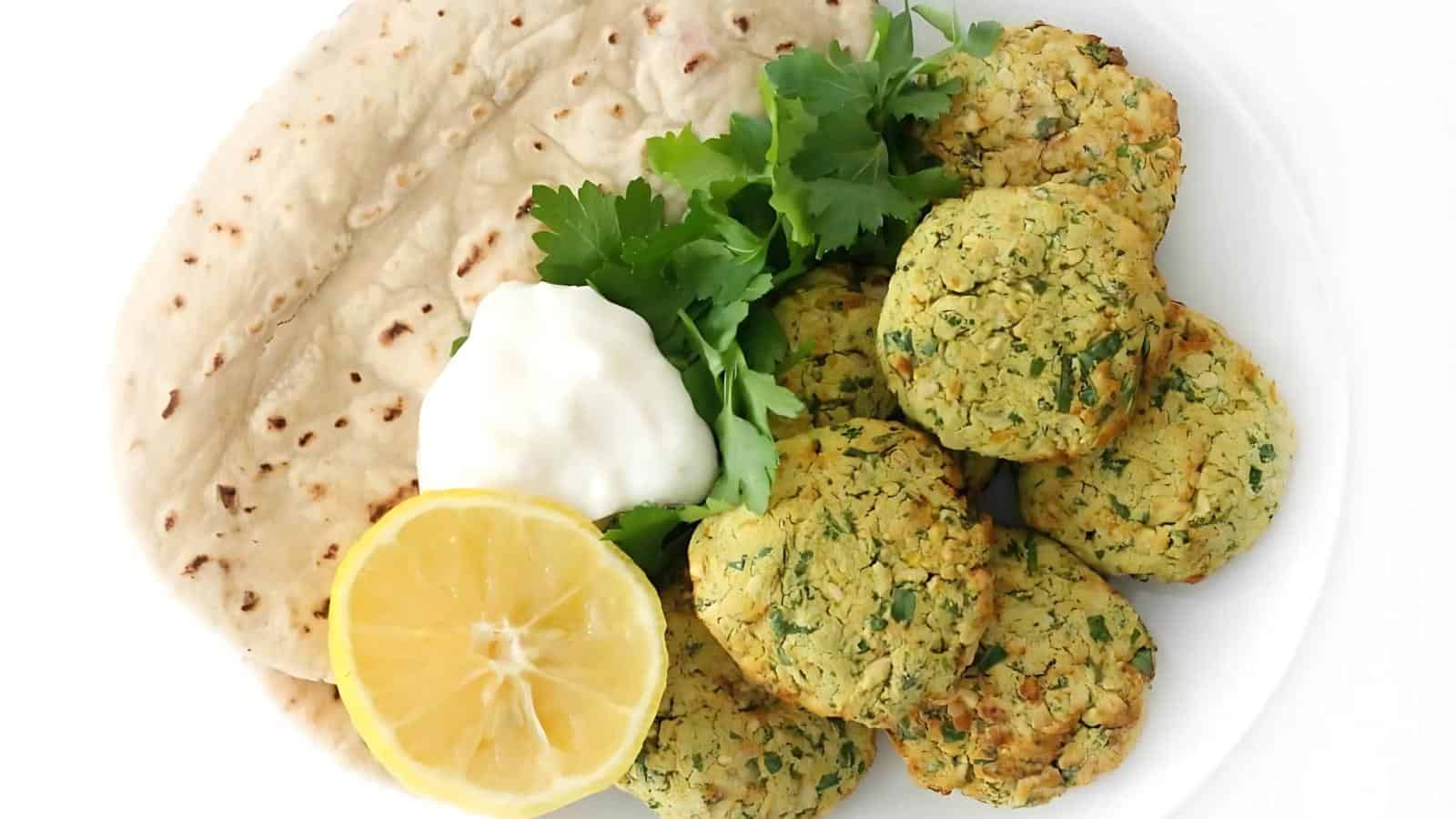 Plate with falafel, flatbread, a lemon half, fresh parsley, and a dollop of white sauce.