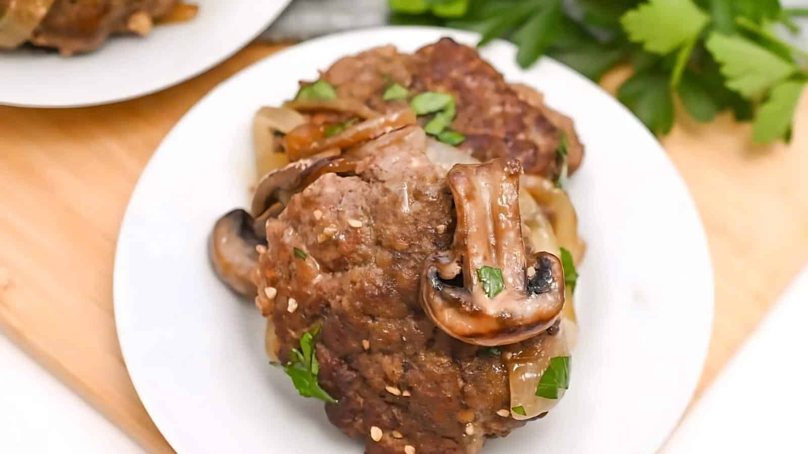 A cooked beef patty topped with sautéed mushrooms and onions on a white plate, garnished with fresh parsley.