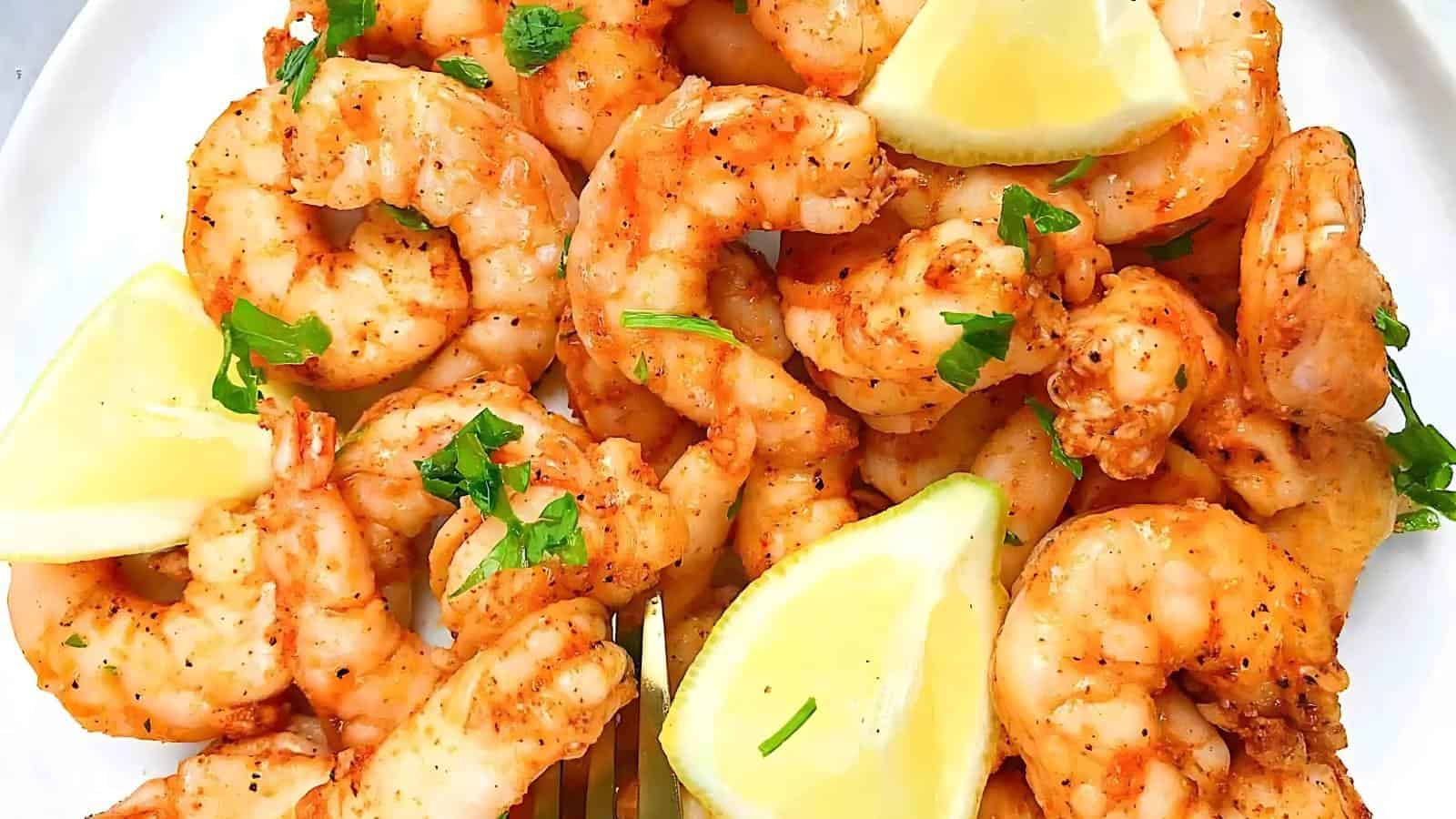 A plate of cooked shrimp garnished with lemon wedges and sprinkled with herbs.