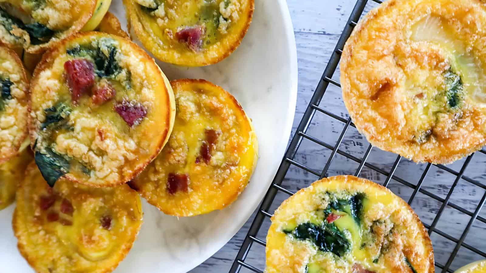 Egg muffins with spinach, cheese, and tomatoes on a white plate and cooling rack.