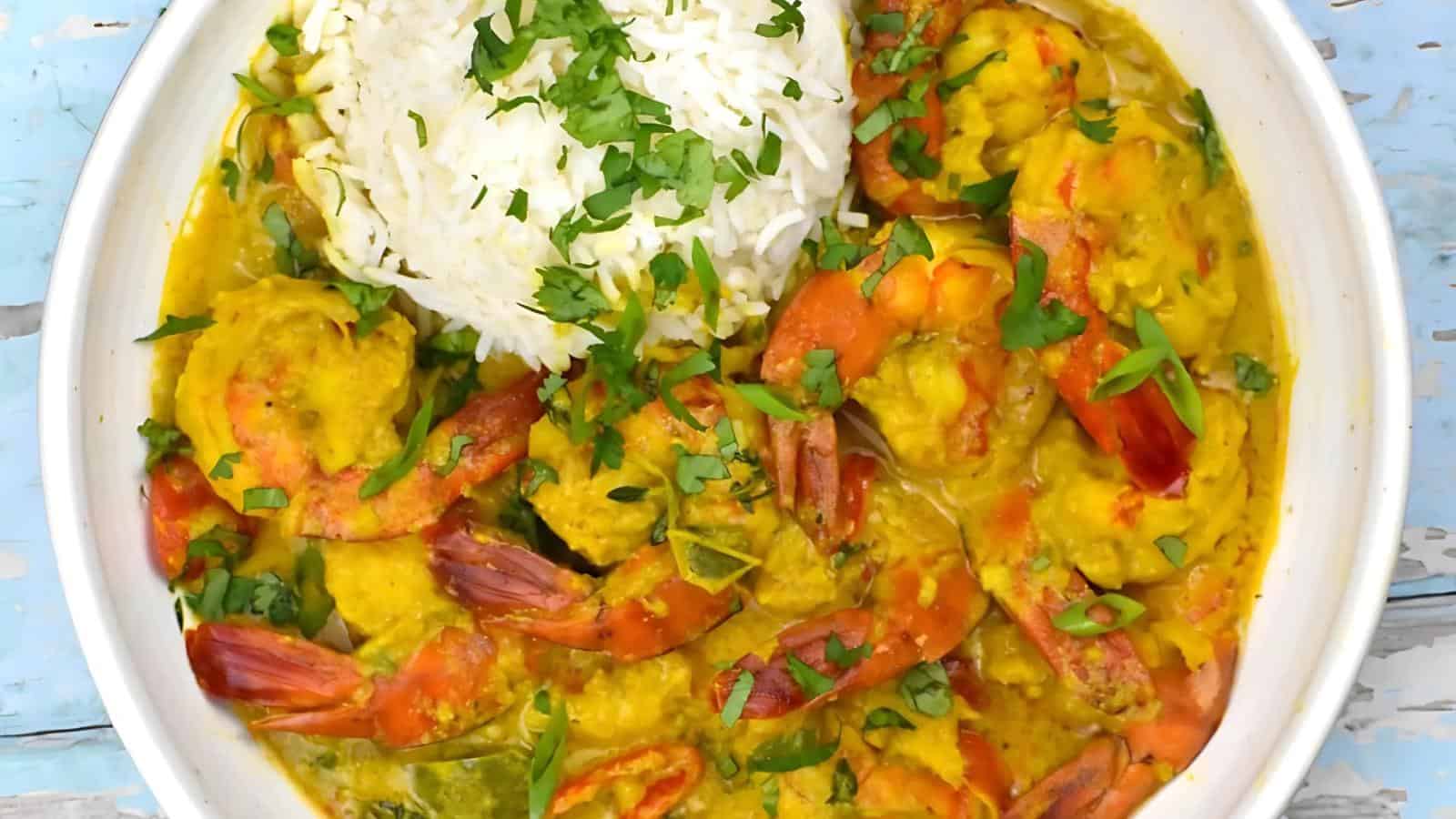 A plate of prawn curry in yellow sauce with a serving of white rice, garnished with chopped parsley.