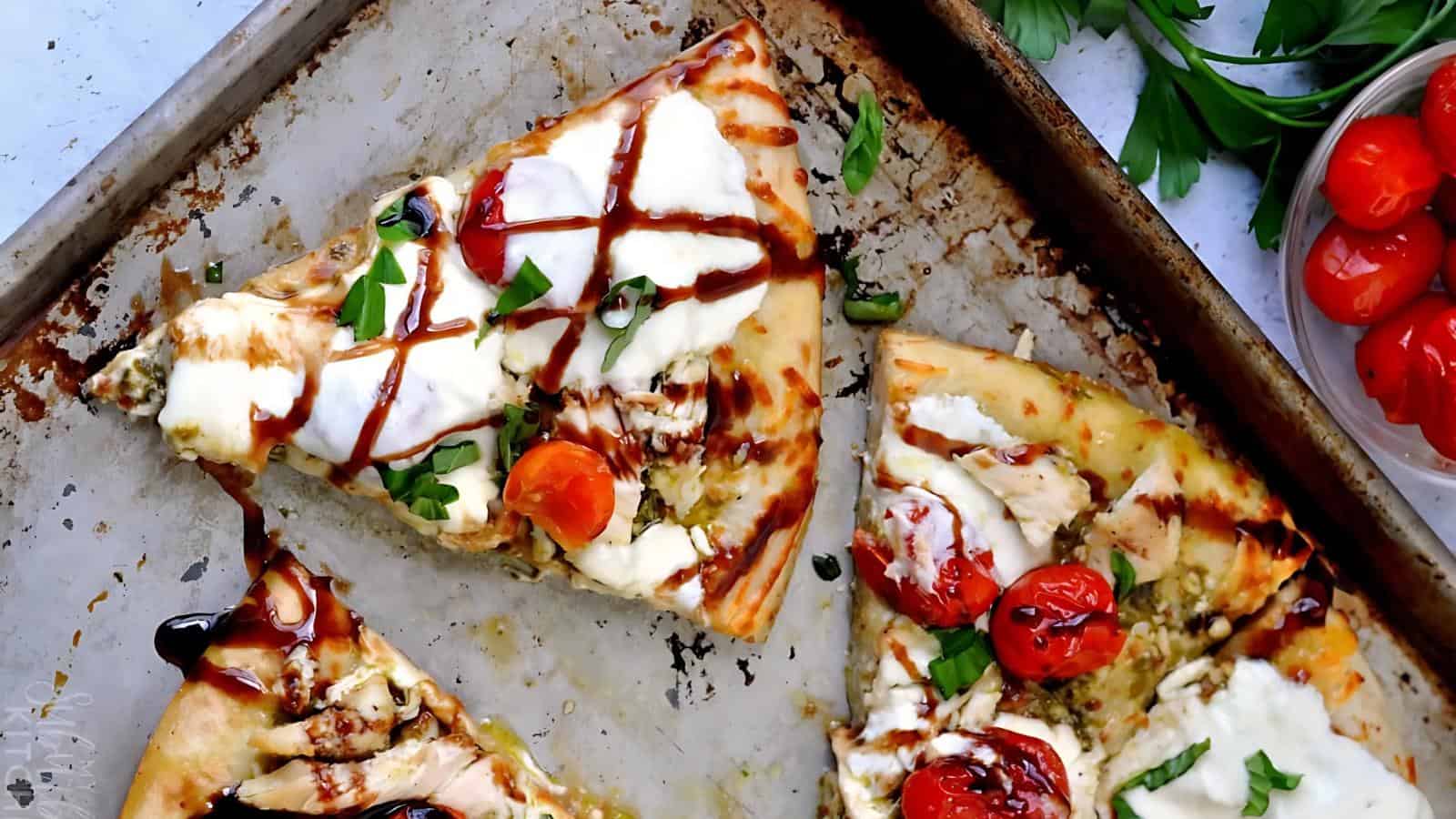 Three slices of gourmet pizza on a baking tray, topped with mozzarella, cherry tomatoes, fresh basil, and drizzled with balsamic glaze.