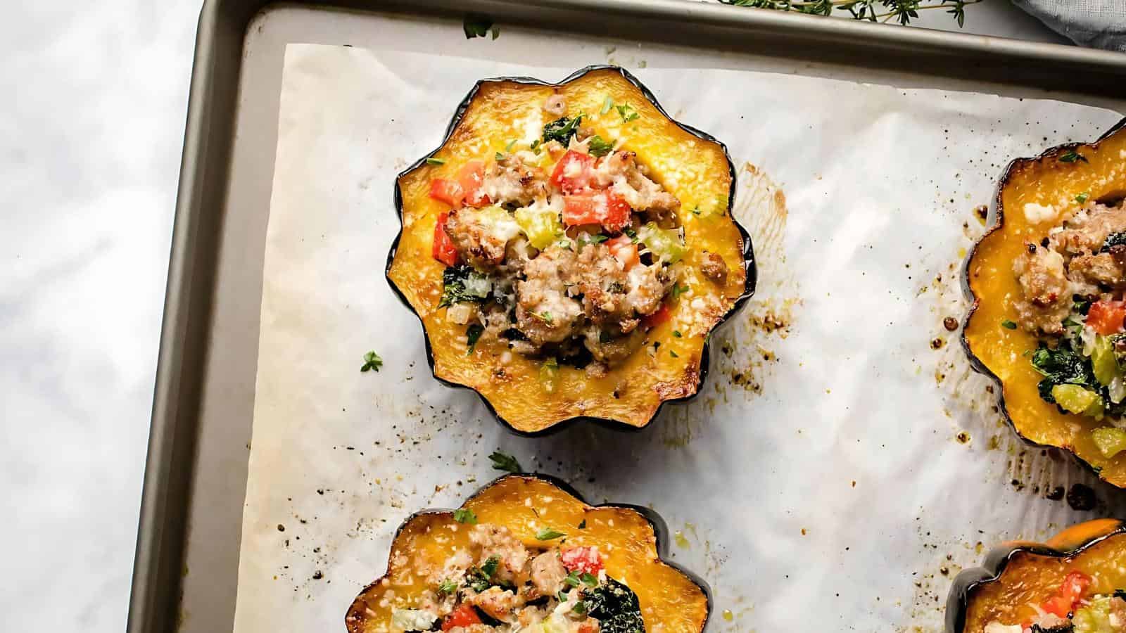 Baked stuffed acorn squash halves on a baking sheet with a savory filling of sausage, vegetables, and herbs.