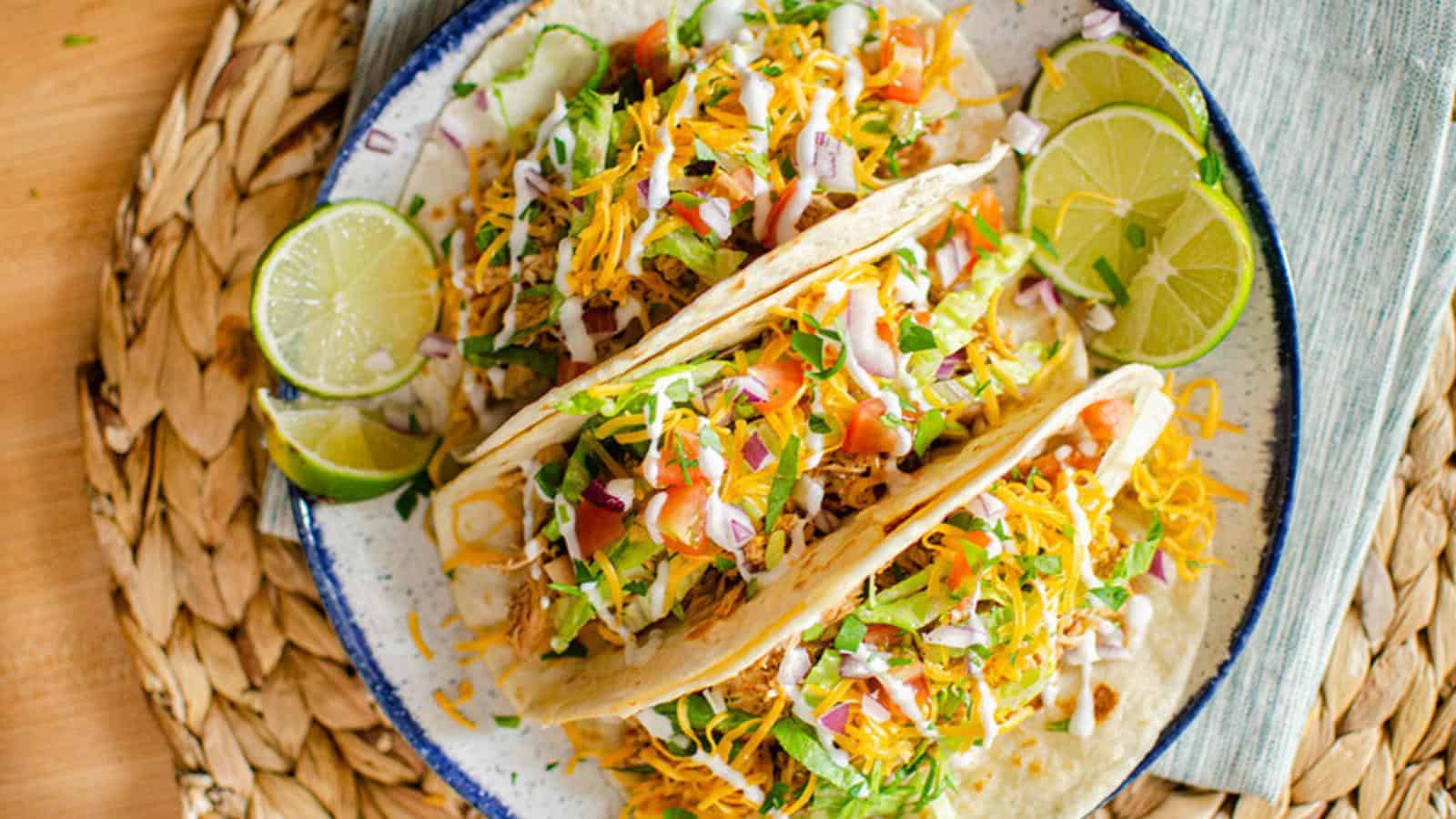 Two tacos filled with shredded lettuce, cheese, diced tomatoes, and onions on a plate, garnished with lime slices.