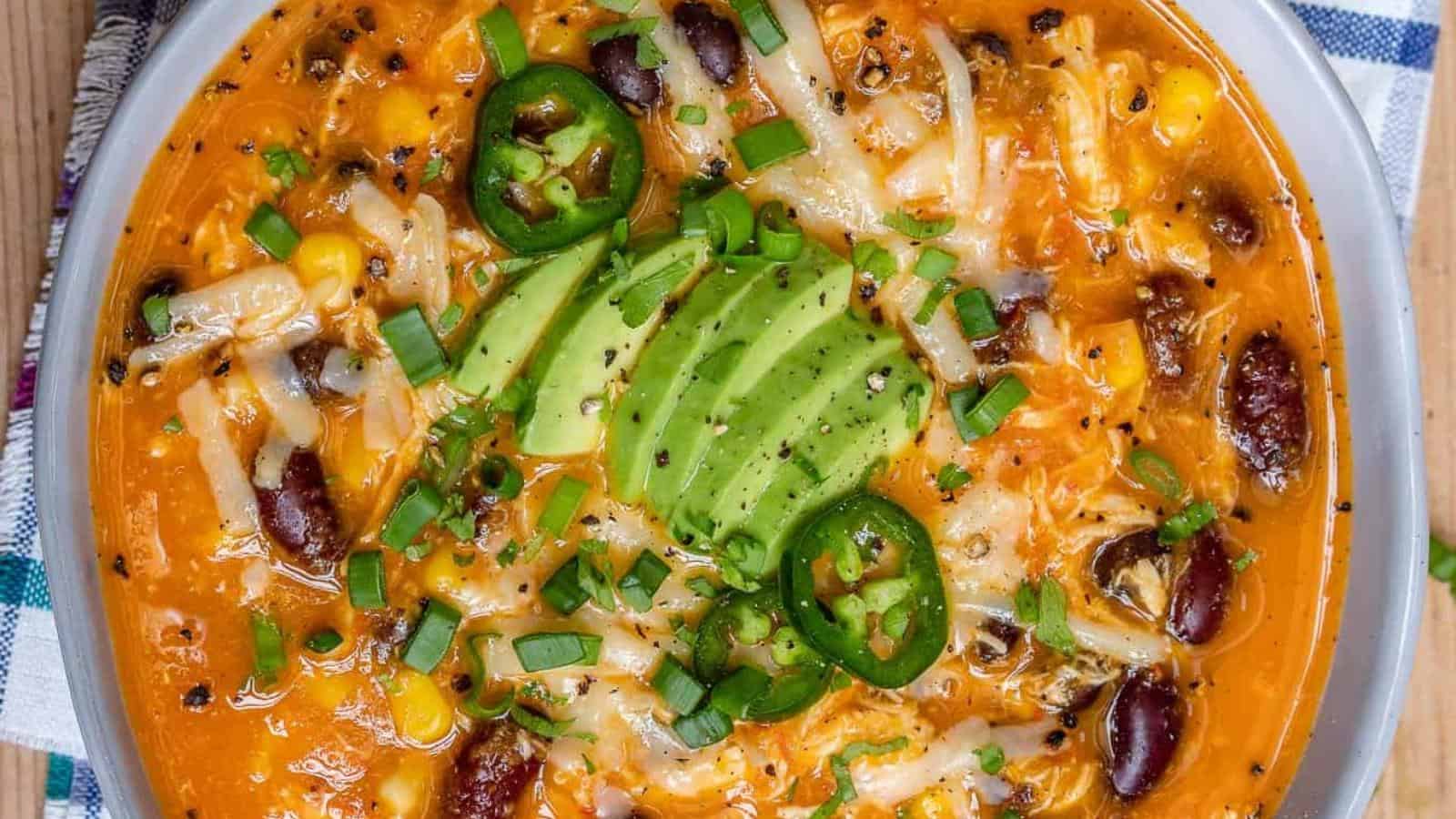 Bowl of chili with melted cheese, avocado slices, jalapeño, kidney beans, corn, and green onions.
