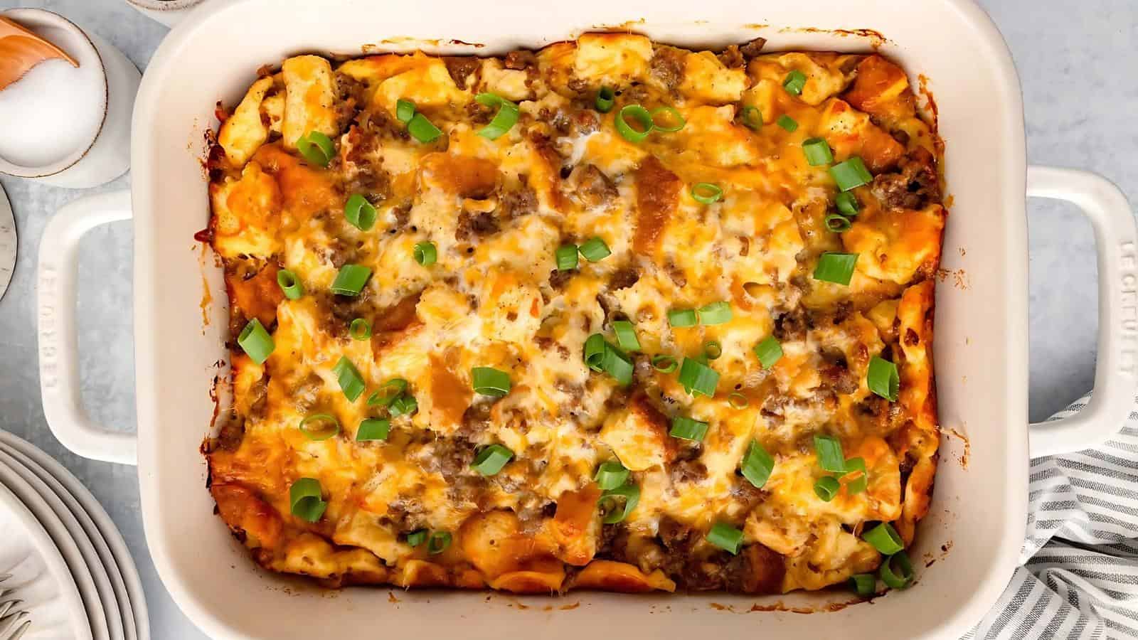 A baked casserole with pasta, melted cheese, ground meat, and chopped green onions in a rectangular dish.