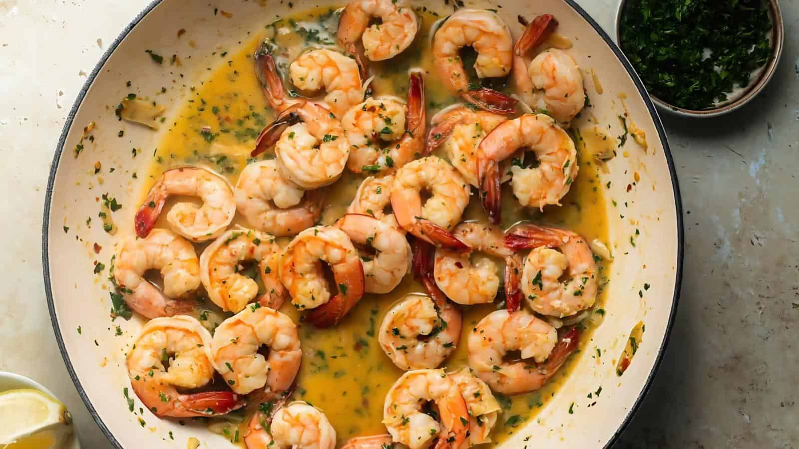 A pan filled with cooked shrimp in a garlic butter sauce, garnished with chopped herbs.