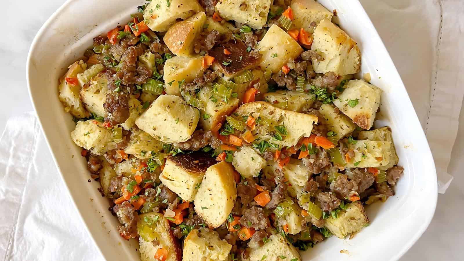 A white baking dish with stuffing containing bread cubes, sausage, carrots, celery, and herbs.
