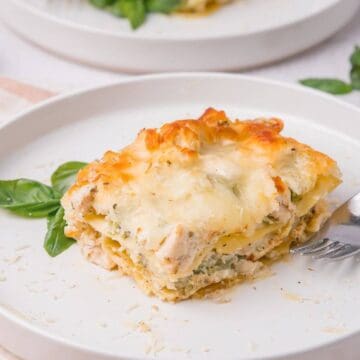 A plate of creamy lasagna topped with melted cheese and garnished with basil next to a fork.