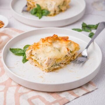A plate with a partially eaten piece of lasagna, garnished with basil leaves. A fork rests on the plate.