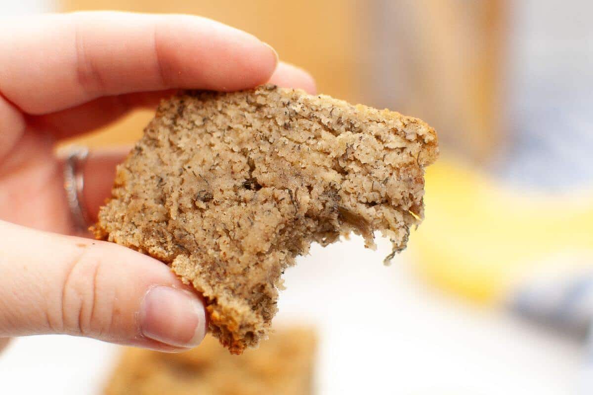 A hand holding a partially bitten slice of banana bread.