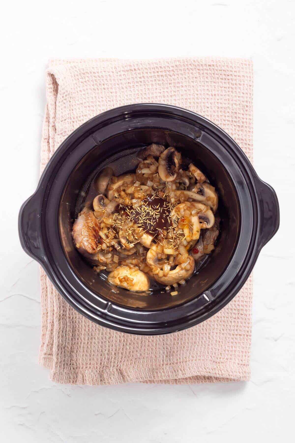 A black pot filled with cooked shrimp and mushrooms in a brown sauce, placed on a folded beige cloth.